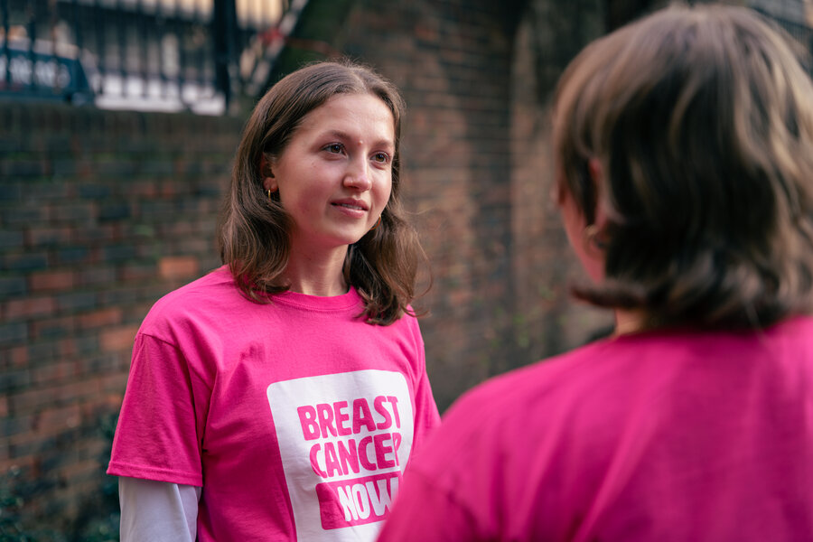 Breast Cancer Now staff wearing merchandise. Two young women talking outside, wearing bright pink Breast Cancer Now cotton t-shirts.