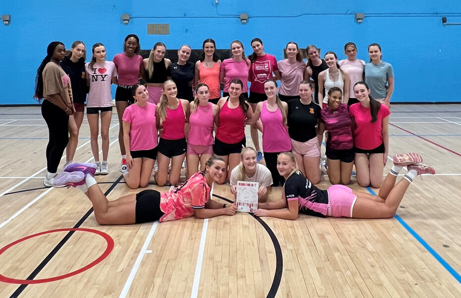 A team of women athletes in a gymnasium, all dressed in pink