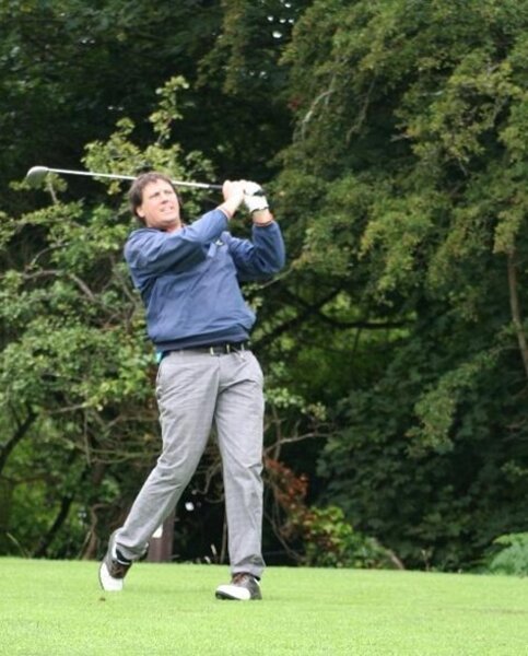 A photo of Kevin playing golf. He is wearing light grey trousers and a long sleeve blue top.