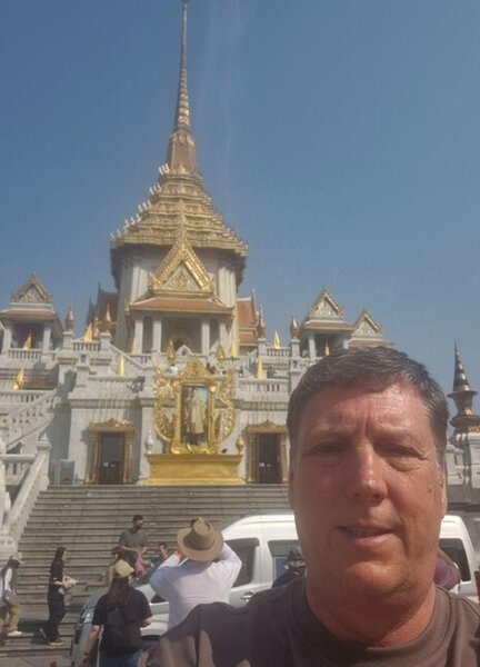 A selfie of a man on holiday standing in front of an impressive white and gold building