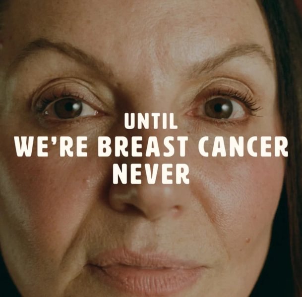 A close up of a woman's face showing her eyebrows, eyes, nose and mouth. There is text over her face saying 'Until we're Breast Cancer Never'. This is a still from an advert from Breast Cancer Now.
