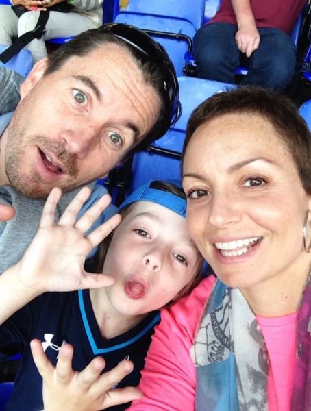 A selfie of a young family made up of a mum, dad and son. They are sitting in the stands of a stadium at an event and smiling at the camera.