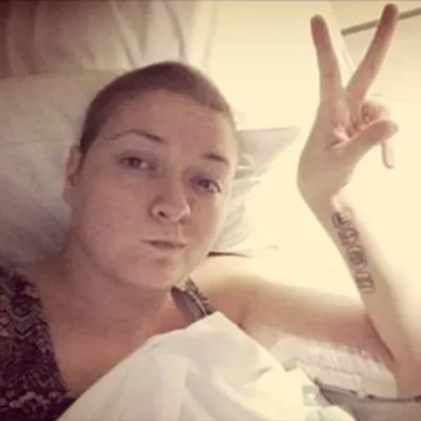 Photo of Vicki with short hair. She is in bed and making a peace sign.