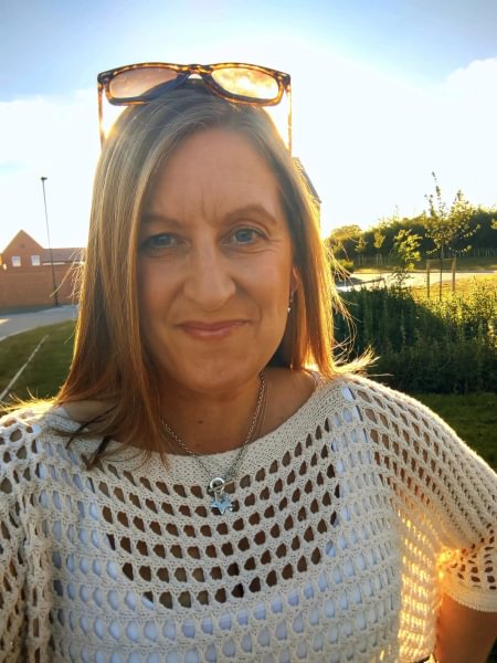 A selfie of Joe standing outside in a garden. The sun is shining behind her and she's wearing a white knitted jumper.