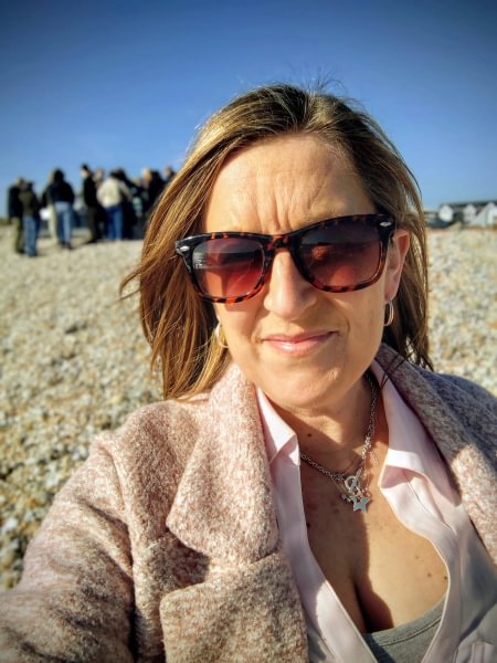 A selfie of Jo on a pebble beach wearing sunglasses.