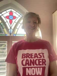 Vicki standing inside in front of a stained glass window. She is wearing her pink Breast Cancer Now t-shirt and is smiling at the camera.