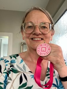 A selfie of Catriona holding a pink medal with the text 'Walk 100 miles' and the Breast Cancer Now logo on it.
