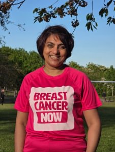 Urmi standing in a park in the evening sun. She is wearing a pink Breast Cancer Now T-shirt.