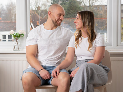 Alex and her partner Ben infront of a window smiling to the camera