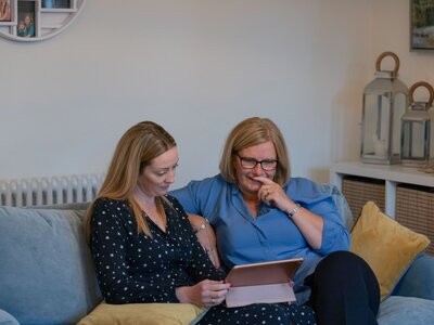 Philippa (in a navy blue top with small stars) and Wilma (in a light blue blouse), sat on a sofa together looking at an ipad.