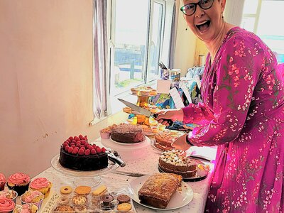 Jess wearing pink next to a table with bakes and cakes