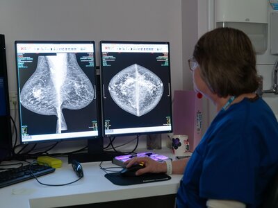 Karen, a consultant radiographer, with short dark hair and glasses, next to a computer screen in a dark room, looking at x-rays of breasts taken in the mammography suite.
