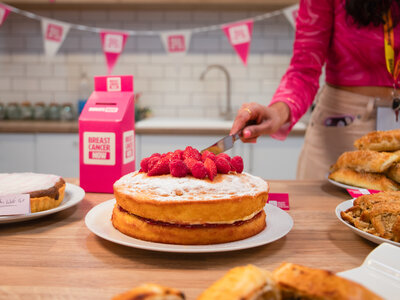 Wear It Pink 2026 in the Breast Cancer Now office, London. Featuring cakes, samosas, biscuits, sweet and savory snacks, and a pink cardboard money box, set against a white office kitchen.