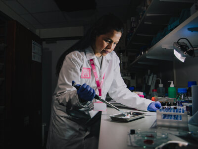 A photo of a researcher wearing a lab coat and a Breast Cancer Now lanyard performing an experiment in a laboratory.