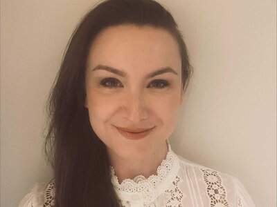 A photo of Lauren, who has long dark hair, is wearing a white blouse and is smiling.