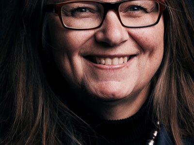 A photo of Veronica smiling at the camera. She has brown shoulder length hair and is wearing a navy blazer.