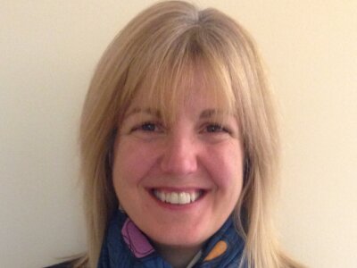 Headshot of Amanda Taylor. She is wearing a navy jumper and a blue scarf with colourful hearts. She's smiling at the camera