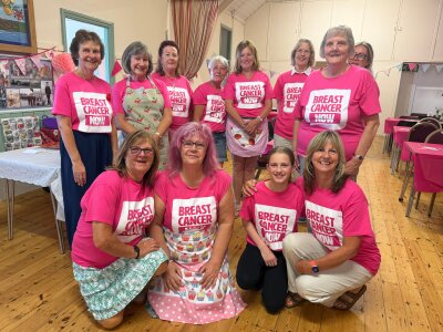 Group photo of people at an Afternoon Tea event wearing pink Breast Cancer Now t-shirt and smiling. In the background are tables with pink tablecloths, and bunting.