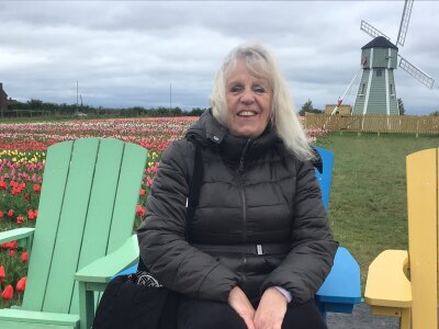 A woman sitting on a wooden chair in front of colourful tulips in the Netherlands with a typical Dutch windmill in the background.