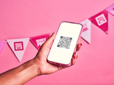 A hand holding a phone with a QR code and pink backdrop with bunting.