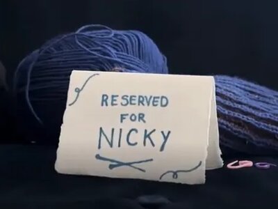 A photo of a handwritten card on a sofa that reads "Reserved for Nicky". Behind it are some cushions and some knitting.