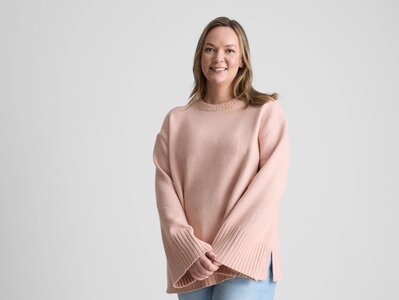 A woman wearing a pale pink knitted jumper and jeans.