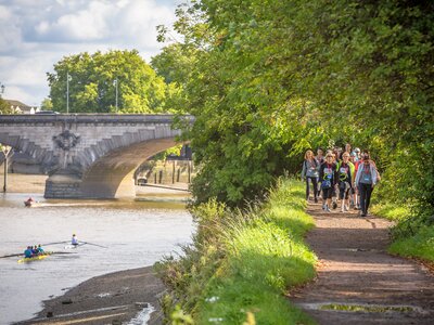 A photo of a group of people walking along a path beside the River Thames on a sunny day as they take part in the Thames Path Challenge.