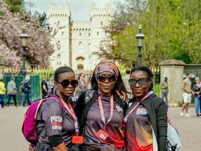A photo of 3 women, who are taking part in the Windsor 50 Ultra Challenge, smiling and standing in front of the gates of Windsor Castle.