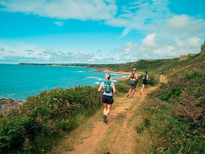 A photo of people running along a coastal path on a sunny day as part of the Gower Peninsula Ultra Challenge