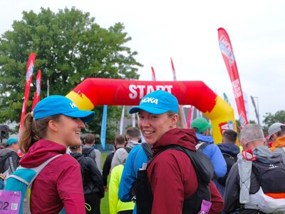 Photo of a group of people at the start line of the Lake District Ultra Challenge. There are 2 women in the foreground, one of whom is turning back to look at the camera and smile.