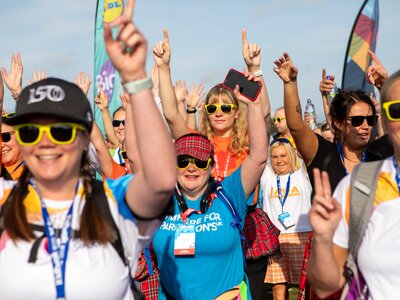A group of participants in the Kiltwalk wearing tartan and putting their hands in the air.