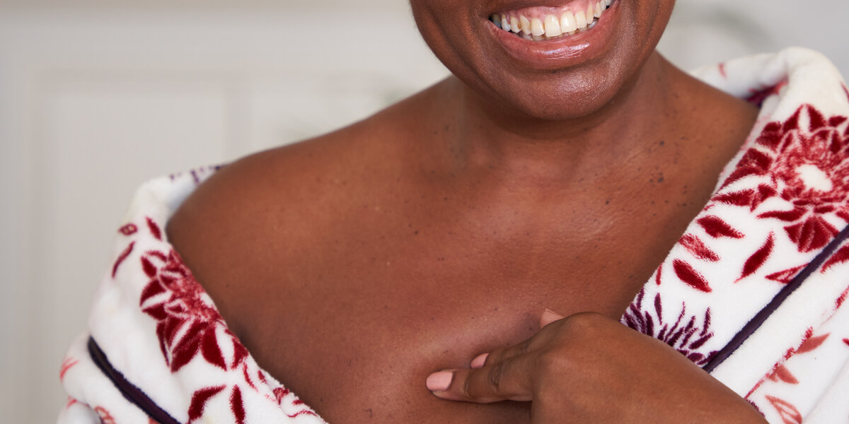 Close up photos of a woman touching her chest, wearing a floral dressing gown in her bedroom.