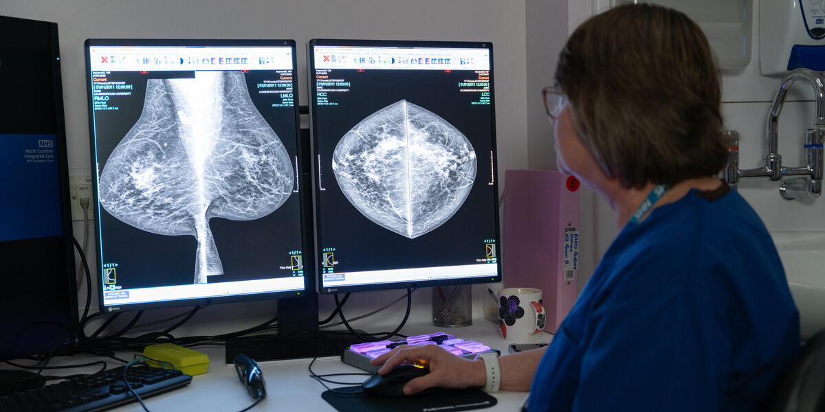 Karen, a consultant radiographer, with short dark hair and glasses, next to a computer screen in a dark room, looking at x-rays of breasts taken in the mammography suite.