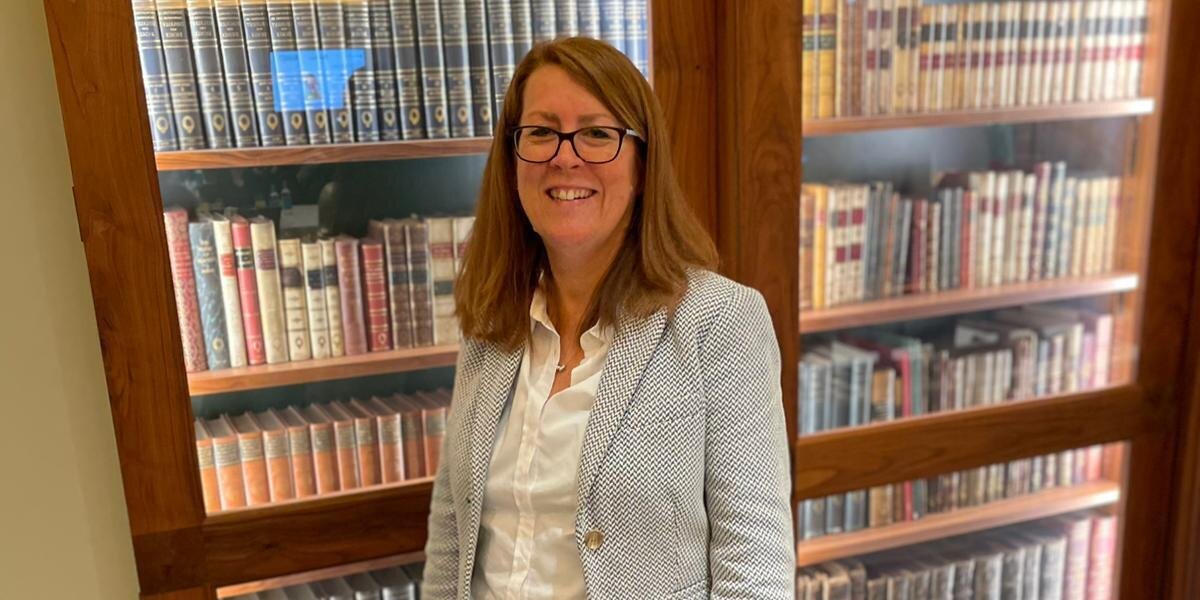 A photo of Professor Clare Foster smiling in front of a bookcase.