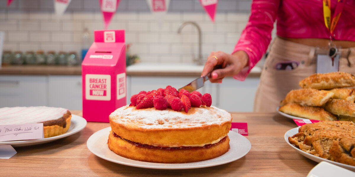 Wear It Pink 2026 in the Breast Cancer Now office, London. Featuring cakes, samosas, biscuits, sweet and savory snacks, and a pink cardboard money box, set against a white office kitchen.