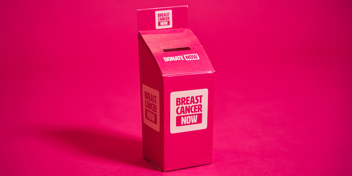 Breast Cancer Now paper pop-up collection donation box on a plain pink backdrop.