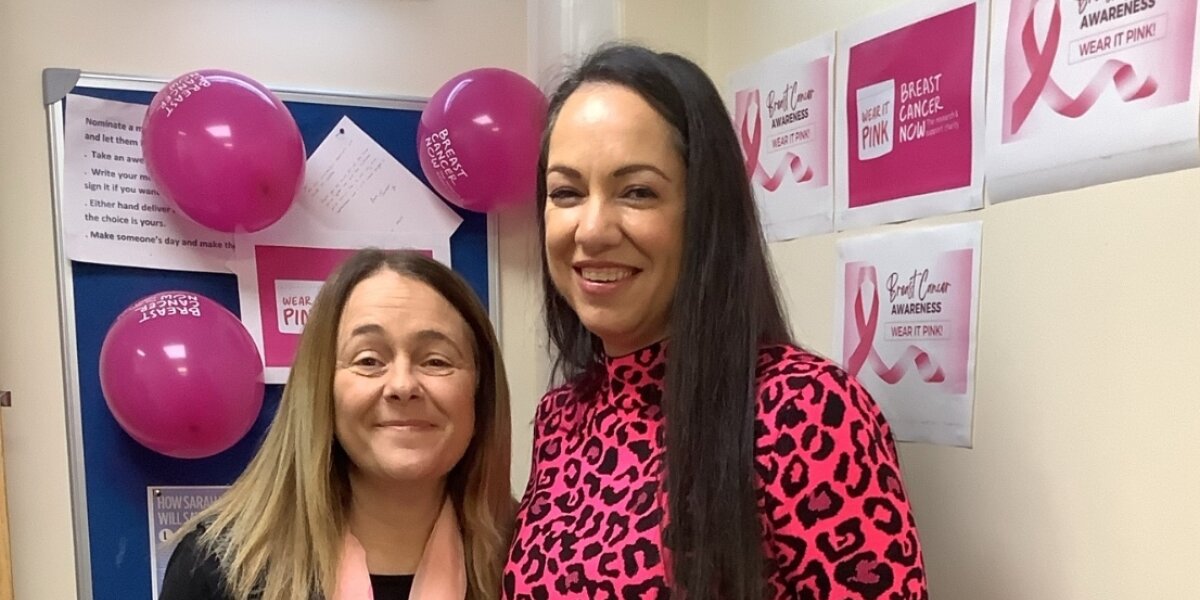 Two women wearing pink and surrounded by Breast Cancer Now posters for Wear It Pink.
