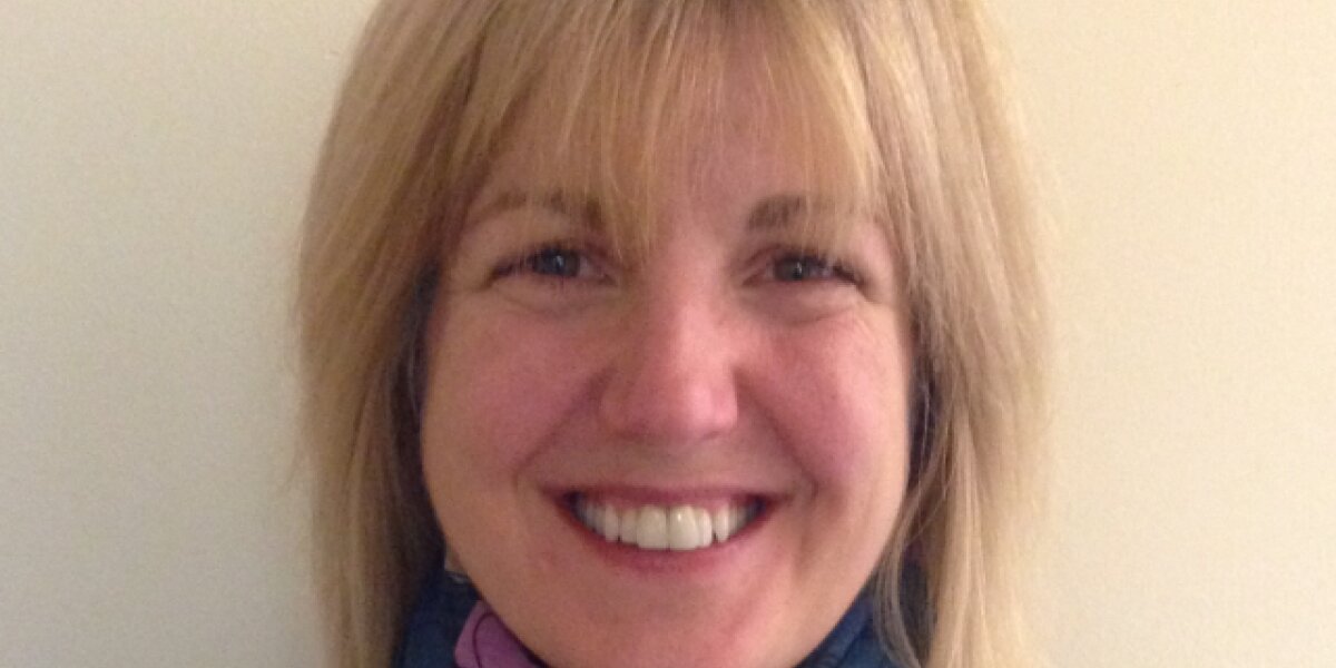 Headshot of Amanda Taylor. She is wearing a navy jumper and a blue scarf with colourful hearts. She's smiling at the camera