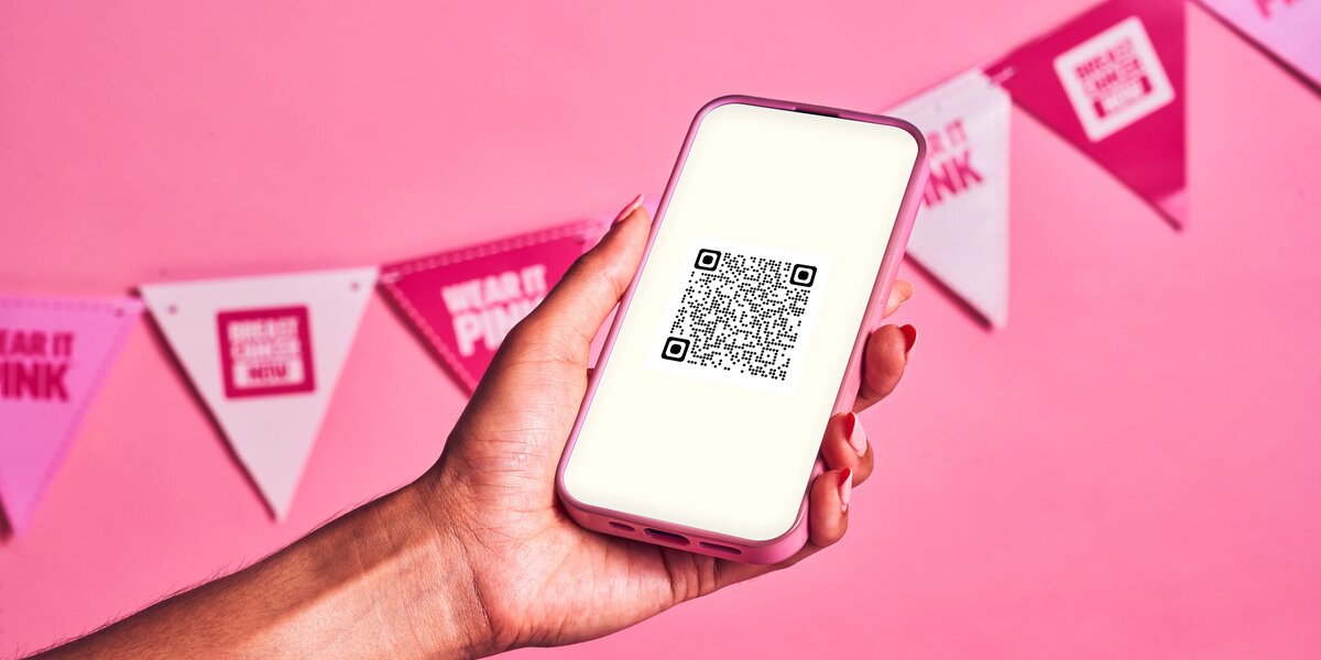 A hand holding a phone with a QR code and pink backdrop with bunting.