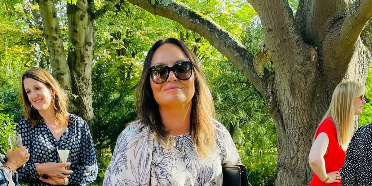 Vickie wearing a summer dress standing in a garden on a sunny day. She's smiling at the camera.