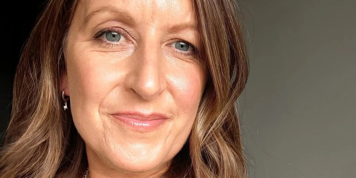 Selfie of Jo against a dark green background and wearing a dark green blouse.