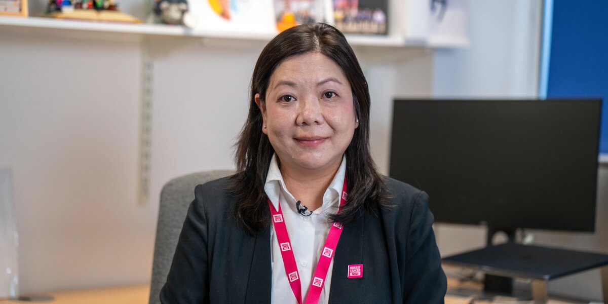 Dr Maggie Cheang, with dark hair, a blazer and pink BCN lanyard, posing for portrait photos in her office.