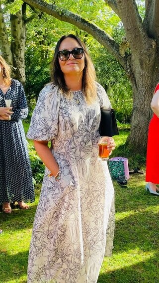 Vickie wearing a summer dress standing in a garden on a sunny day. She's smiling at the camera.