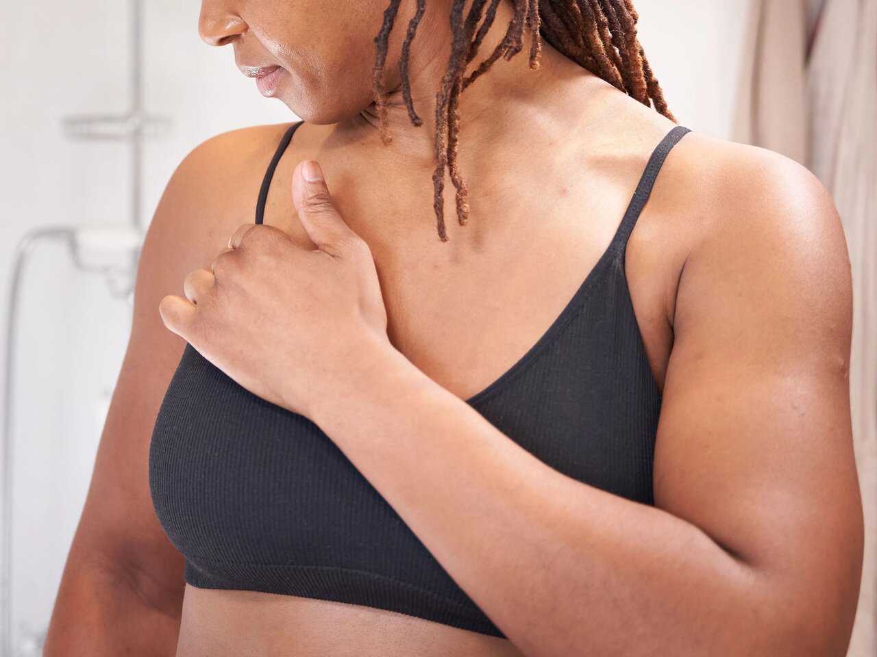 A woman in a black vest top, checking her chest in the bathroom.