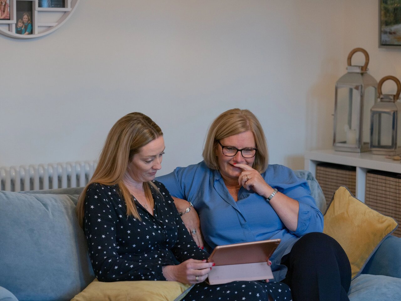Philippa (in a navy blue top with small stars) and Wilma (in a light blue blouse), sat on a sofa together looking at an ipad.