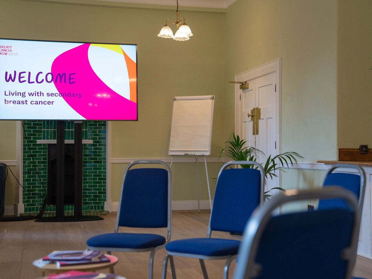 A welcome message on a tv screen in a green room, with chairs organised in a semi circle ready for a support group.