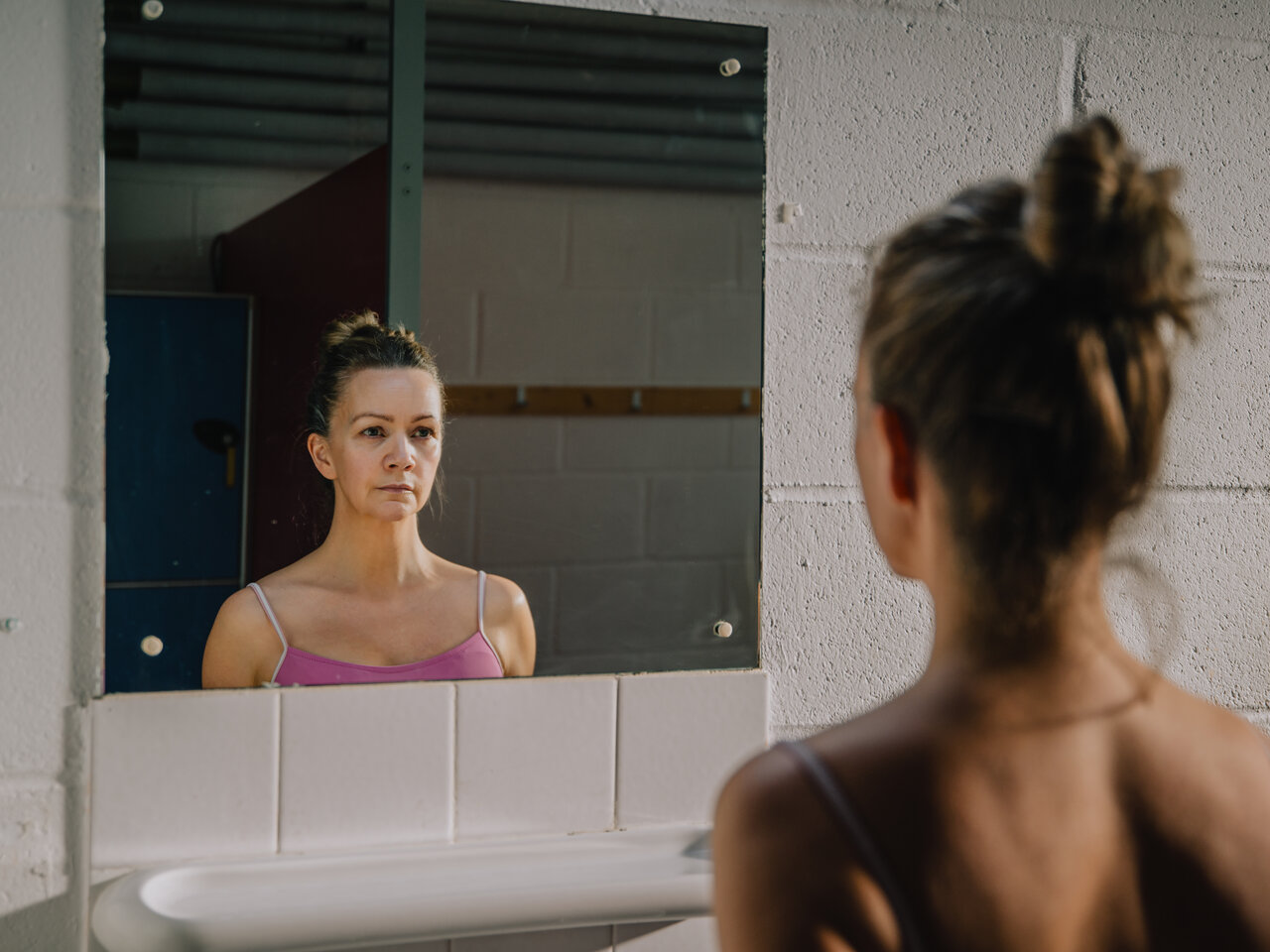 A photo of a woman looking into a bathroom mirror in a changing room.