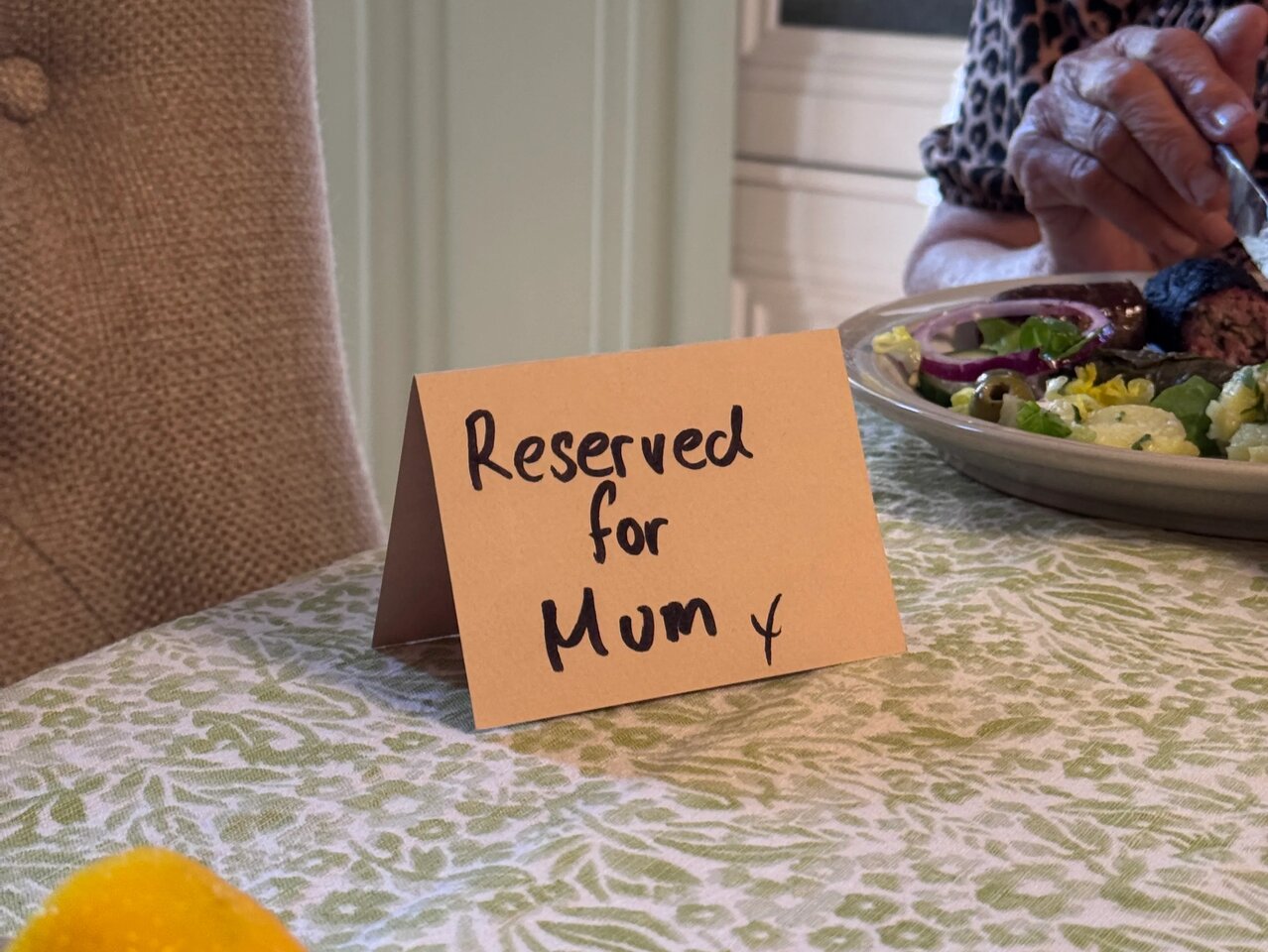 Photo of a card which reads "Reserved for Mum" at an empty space between table settings.
