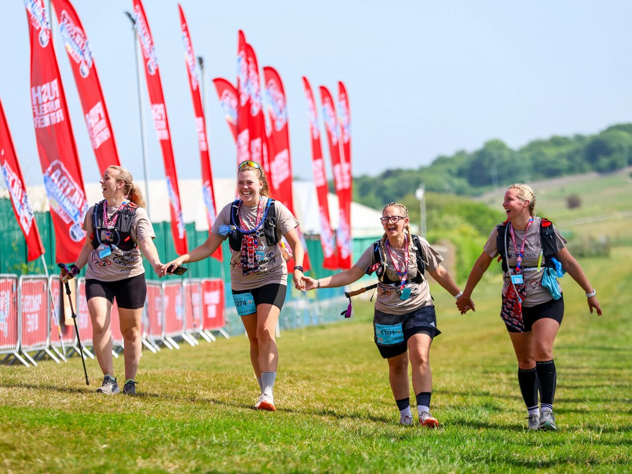 Photo of 4 women wearing walking gear and holding hands as they take part in the Shropshire Hills 50 Ultra Challenge