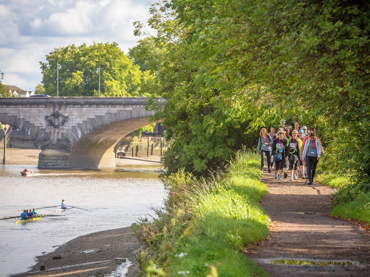 A photo of a group of people walking along a path beside the River Thames on a sunny day as they take part in the Thames Path Challenge.